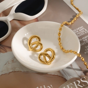 Detailansicht goldener gedrehter Herzohrringe auf Keramikschale mit Modezeitschriften