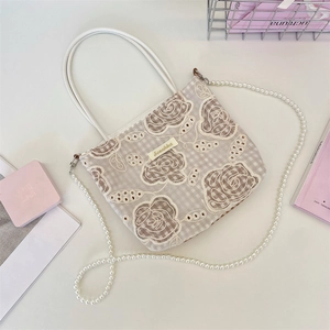 Détail du sac cabas en dentelle florale avec bandoulière perle et logo en métal