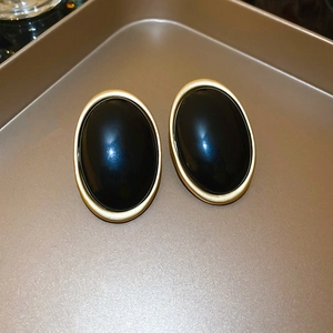 Gros plan sur des boucles d'oreilles ovales en résine noire et cadres dorés mats