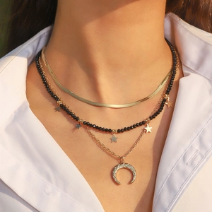 Close-up of gold layered necklace with black beads and sparkling moon and star pendants