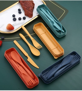 Flat lay of colorful wheat straw cutlery sets with storage cases on a dark green table