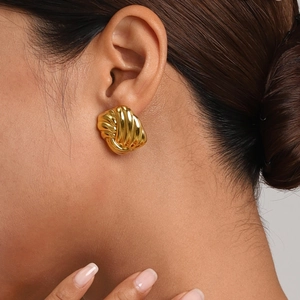 Close-up of a model wearing a gold twisted stud earring with a glossy metallic finish