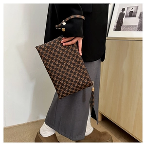 Detail shot of a brown monogram envelope clutch bag with tassel held by a model