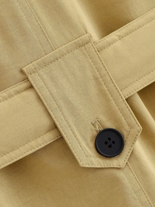 Macro detail of khaki twill fabric with black resin button and precision stitching on jacket