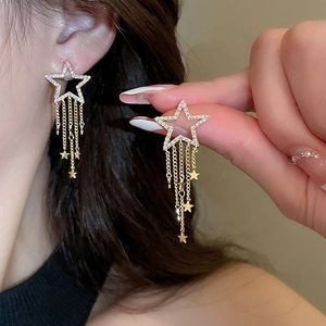 Detailed close-up of gold star tassel earrings with rhinestones on a female model