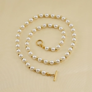 Collier de perles élégant avec billes dorées et fermoir à bascule OT sur tissu beige
