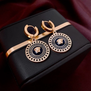 Detail of rose gold Medusa earrings with blue enamel and Greek key border on silk background