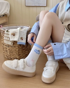 Detail of white crew socks with blue cuffs, pink bows, and happy cloud patterns on model