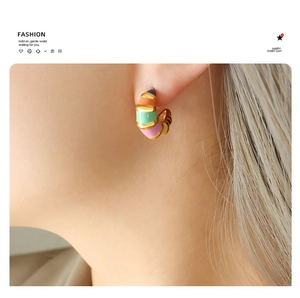 Macro shot of a model wearing colorful striped C-shaped enamel gold hoop earrings
