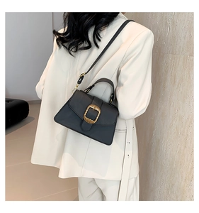 Detail view of black vintage square crossbody bag with gold textured buckle and white suit