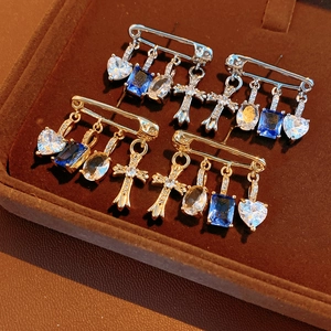 Detail of safety pin earrings with zircon heart, cross, and blue rectangle charms
