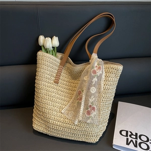 Dettaglio borsa tote in paglia intrecciata con spalline in PU e tulipani su un divano