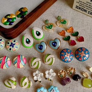 Flat lay of vintage colorful enamel heart and flower earrings on a textured fabric