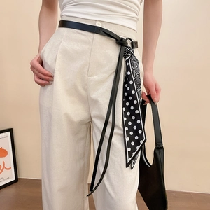 Détail d'une fine ceinture en cuir noir ornée d'un foulard en soie à pois élégant