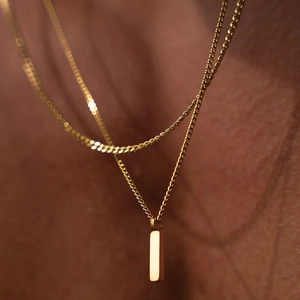 Dettaglio di una collana minimalista in acciaio inossidabile dorato con pendente a barra
