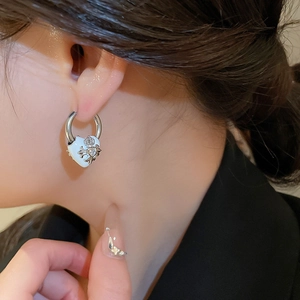 Nahaufnahme eines silbernen Creolen-Ohrrings mit weißem Herz-Anhänger und Kreuz-Kronen-Motiv