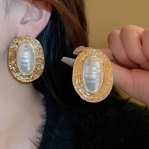 Close-up of vintage gold pleated oval earrings with white pearls on a model