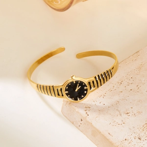 Detail of a minimalist gold watch-style open cuff bracelet on a natural stone surface