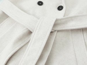 Close-up of oatmeal wool coat fabric showing soft texture, round black buttons and waist belt