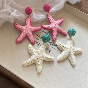 Close-up of pink and beige raffia woven starfish earrings for a beach vacation style