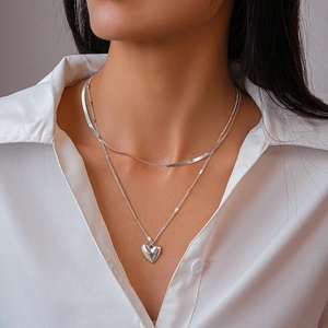Double-layered silver necklace with snake chain and heart pendant on white shirt
