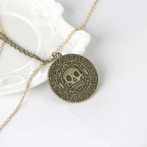 Vintage bronze and gold skeleton pendant necklace with Aztec calendar design on white tray