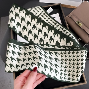Detail view of a green houndstooth skinny silk scarf draped over a beige handbag