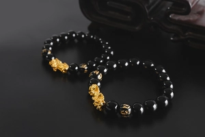 Macro detail of obsidian beads with gold mantra carvings and a golden Pixiu charm