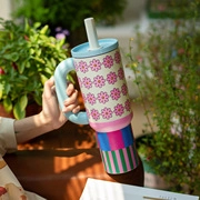 Close-up of a hand holding a floral diatomite mug with colorful stripes and a blue lid