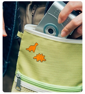Dettaglio di spille in smalto a forma di dinosauro arancione su borsa di tela