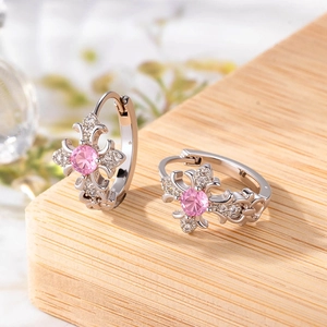 Silver cross earrings with pink zircons and small clear stones on a wooden background
