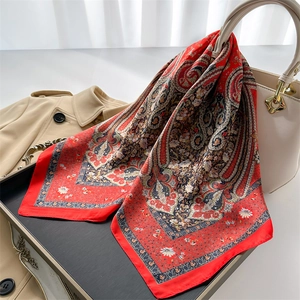 Elegant red paisley silk scarf draped over a white handbag and trench coat background