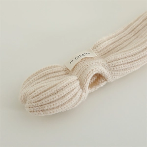 Detail of beige chunky knit scarf with ribbed texture and woven brand label