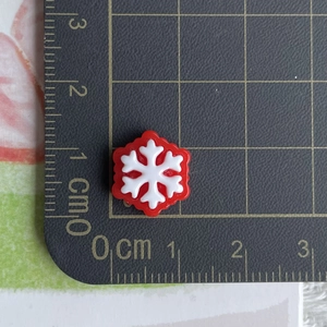 Detailed close-up of a 1.2cm mini red and white snowflake resin charm on a scale mat