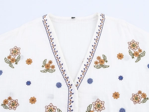 Detailed view of colorful floral embroidery and V-neckline on white cotton blouse