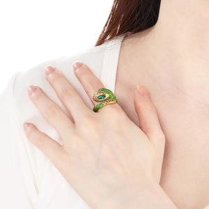 Macro detail of golden snake ring with green enamel scales and gemstone eyes on finger