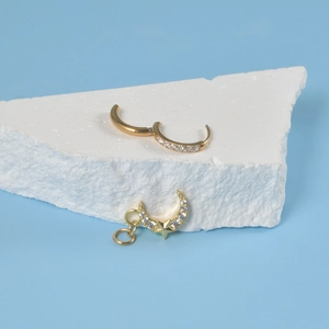 Detailed close-up of golden moon and star charm huggie hoop earrings with white zircon stones
