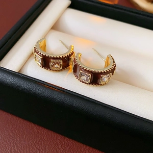 Close-up of gold-plated C-shaped earrings with brown enamel and square crystals in a box