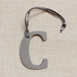 Detailed view of grey pebble leather letter C bag charm on a beige linen background