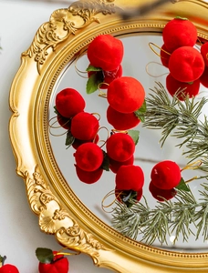 Close-up of festive flocked red apple ornaments with green leaves on a vintage gold tray