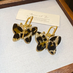 Detailed close-up of leopard print butterfly pendant earrings with golden hoops