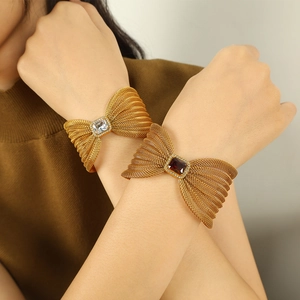 Elegant gold bow cuff bracelets with sparkling zircon and deep red gemstone on hands