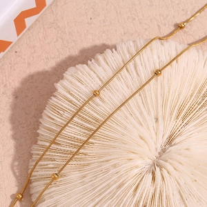 Detailed close-up of 18K gold-plated double-layer bead and snake chain bracelet on coral