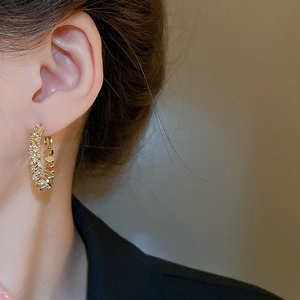 Gros plan de boucles d'oreilles créoles C dorées avec zircons portées par un mannequin