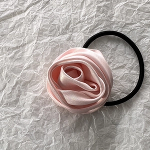 Detailed view of pink satin rose flower hair tie with high elastic black band on white paper