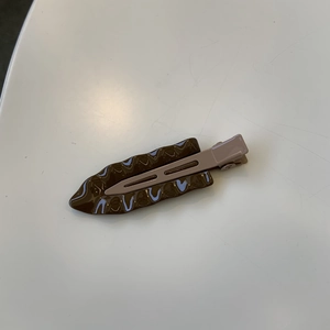 Macro detail of leaf-shaped hair clip in dark brown with glossy wavy texture finish