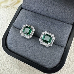 Detail of emerald cut green gemstone earrings in silver halo setting on grey velvet tray