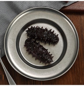 Detail shot of two sea cucumbers on a vintage stainless steel snowflake soup plate