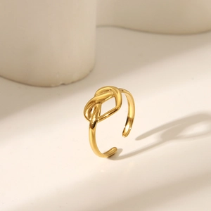 Bague ouverte à nœud doré poli avec anneau ajustable sur des accessoires géométriques blancs
