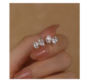 Macro shot of silver bow stud earrings with sparkling zircon stones held by fingers